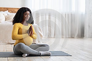 Peaceful black pregnant lady meditating at home