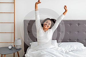 Peaceful black woman stretching arms and back sitting on bed