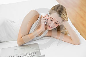 Peaceful blonde woman phoning while lying on her bed
