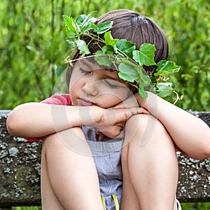 Peaceful child with foliage crown closing her eyes to sleep