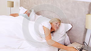 Peaceful couple sleeping in bed with woman turning off alarm