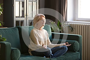 Calm senior woman meditating on couch at home