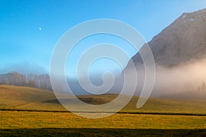 Peaceful foggy landscape with hill above the meadow of horizontal lines under the blue sky
