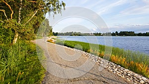 A peaceful footpath along the coast of a lake during sunset in summer with beautiful green vegetation