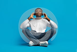 Peaceful handsome young african guy listening to music on blue