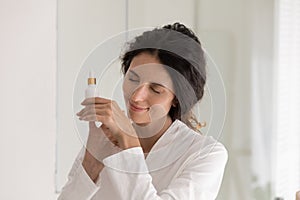 Peaceful happy young woman applying oil perfume on hands.