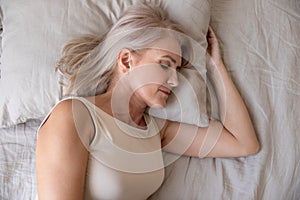 Peaceful healthy mature woman lying asleep in bed, top view
