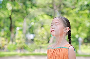 Peaceful little Asian child girl close their eyes in garden with Breathe fresh air from nature. Portrait of kid relax in green