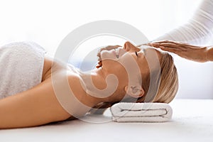 Peaceful middle aged woman getting gentle acupressure head massage in spa salon