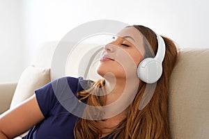 Peaceful millennial girl lie on comfort couch wearing wireless headphones enjoy good meditative music. Serene young woman in