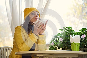 Peaceful millennial multi-ethnic woman in yellow hat and jacket, relaxing, enjoying her weekend in a cozy coffee shop