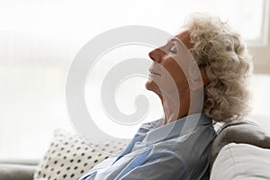 Peaceful old woman leaned on couch breathing fresh conditioned air