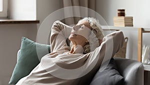 Peaceful older 60s lady resting on comfortable couch