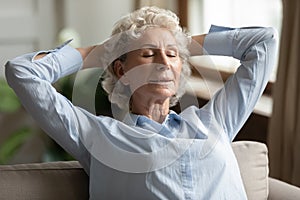 Peaceful older grandma relaxing on couch with closed eyes.