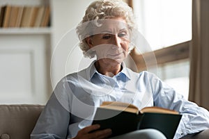 Peaceful older woman reading interesting bestseller paper book.