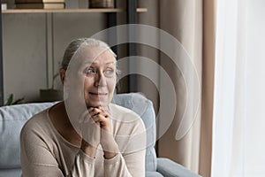 Peaceful older woman sits on couch, smile staring out window photo