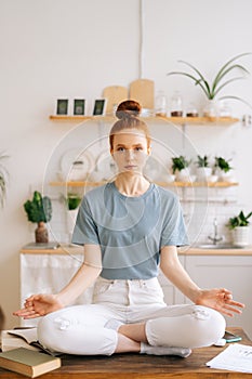 Peaceful redhead young woman is meditating while sitting on desk at home office