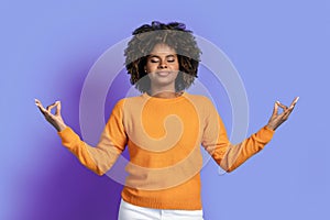 Peaceful relaxed black woman meditating on purple studio background