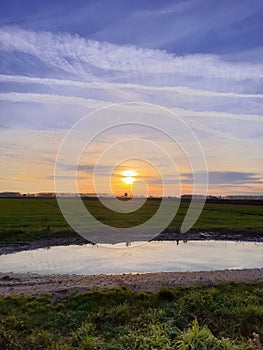 Sunset Over Green Fields with Sky Reflection in Water