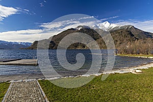 Peaceful scenic view small jetty in European village dock on idyllic calm lake waters surface surrounded by Alps mountain snowy