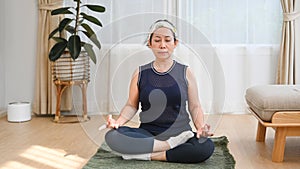 Peaceful senior woman sitting on mat, meditating at home. Retirement, healthy lifestyle concept