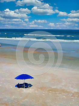 A peaceful and serene beach scene with sand, waves, clouds and umbrella