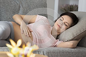 Peaceful sleepy expecting mom resting on couch, caressing bare belly
