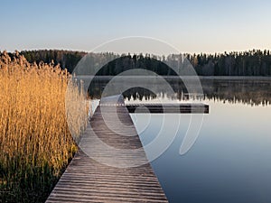 Peaceful spring landscape with a wooden footbridge in the lake, empty beach in the morning