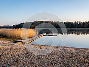 Peaceful spring landscape with a wooden footbridge in the lake, empty beach in the morning