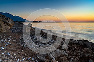 Peaceful sunset over the ocean with silhouette of mountains and pebble beach iwth rock boulders in the foreground