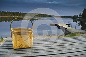 Peaceful tranquill view of nature with lonely wooden bucket sitting on an old wooden table in front of a lake during the summer
