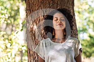 Peaceful woman leaning against a tree with her eyes closed