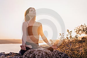 Peaceful yogi woman sitting in lotus, meditating, feeling free in front of wild nature. Mindful fitness coach having zen