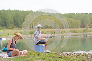 Peaceful young couple fishing by pond in autumn