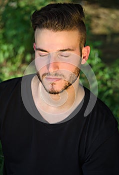 Peaceful young man with eyes closed, relaxing outdoors in nature