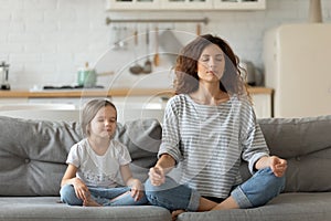 Peaceful young mother and little daughter meditating, doing yoga exercise