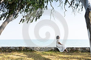 Peacefully, Athletic young asian woman wearing white dress sitting on pier with smiling and happy. View from behind while resting