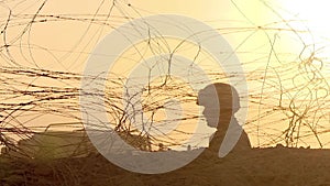 A peacekeeper soldier in a helmet and with a machine gun guarding a checkpoint in the desert, fences and barbed wire, sunrise, sil