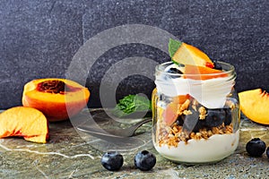 Peach and blueberry parfait in a mason jar against dark stone