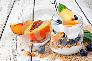 Peach and blueberry parfait in a mason jar with a white wood background