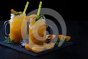 Peach cocktail or tea with ice and mint on a black background