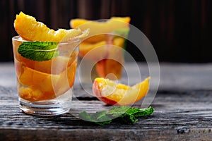 Peach cocktail or tea with mint on wooden background.