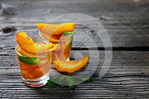 Peach cocktail or tea with mint on wooden background.