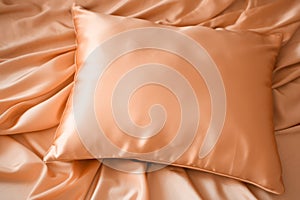 A peach fuzz color satin pillow on silky draped satin background
