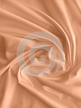Peach fuzz is the color of the year 2024. Silk fabric folded with beautiful curves with shadows, top view.