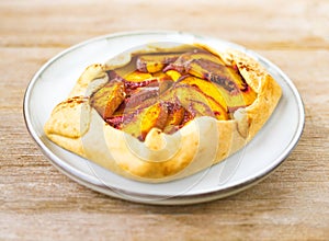 Peach galette on plate on rustic wooden background. Homemade tart open pie with fresh organic fruits