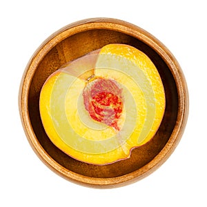 Peach half, cross section of a ripe fruit, in a wooden bowl