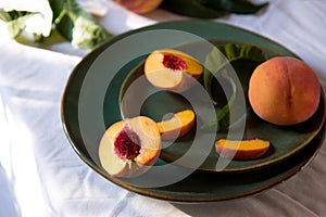 Peach in halves with bone. Peaches with leaves on color green plate on table with white tablecloth. Ripe juicy peaches Still life