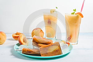 Peach ice cream on a stick in a blue plate and ice cubes, peach refreshing juice in a glass with ice and pieces of fruit and mint