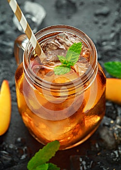 Peach Ice tea with mint in glass jar, on rustic black background. summer fruit cold drinks